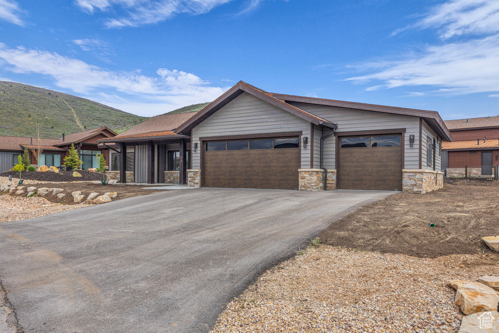 Single story home with stone siding, driveway, a garage, and a mountain view