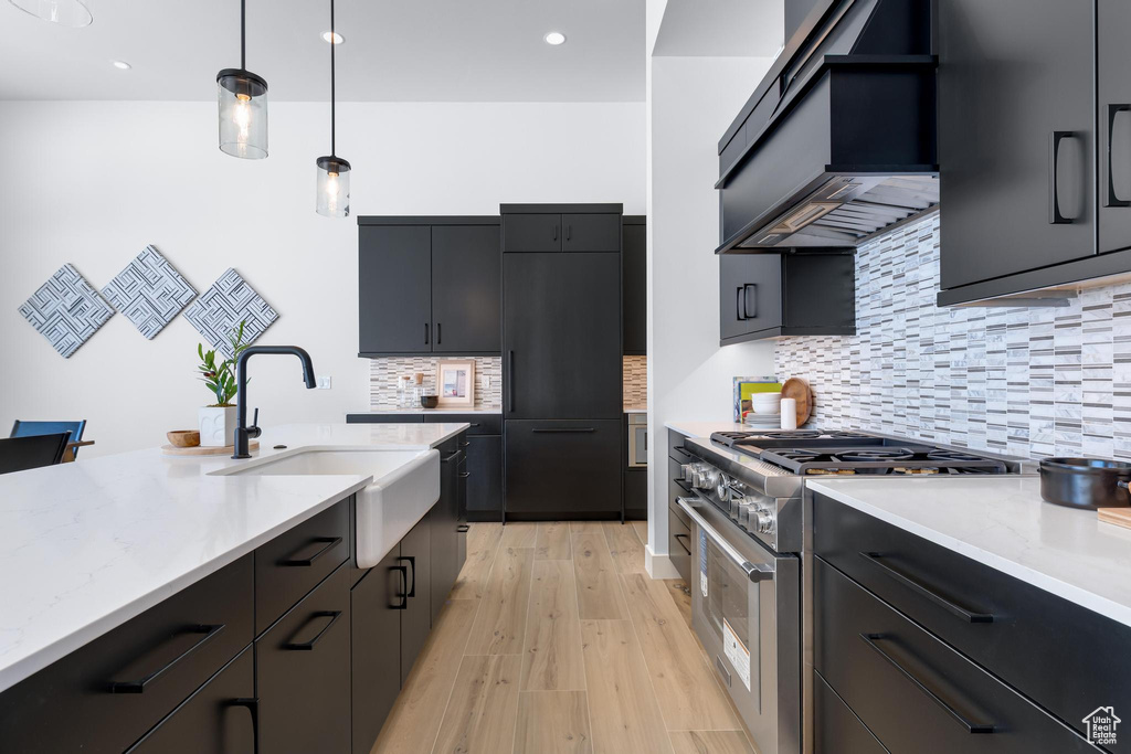 Kitchen with light stone counters, custom exhaust hood, high end stainless steel range oven, hanging light fixtures, and a sink