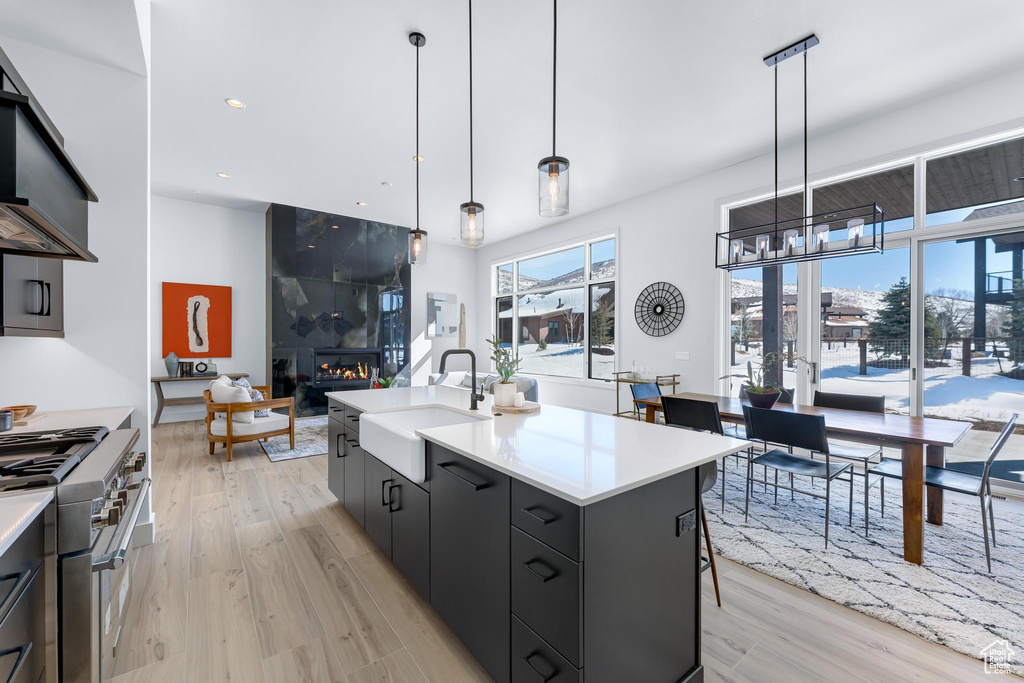 Kitchen with light countertops, high end stainless steel range, a kitchen island with sink, and pendant lighting