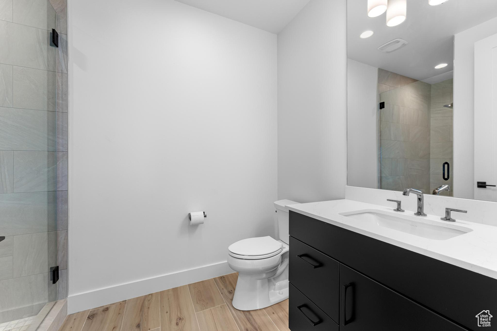 Full bath featuring toilet, wood finished floors, vanity, baseboards, and a stall shower