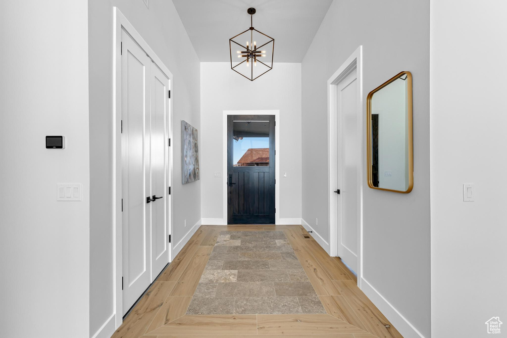 Doorway with baseboards, light wood finished floors, and a notable chandelier