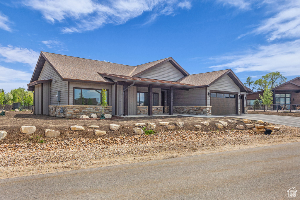 View of front of house with stone siding, concrete driveway, a garage, and a shingled roof