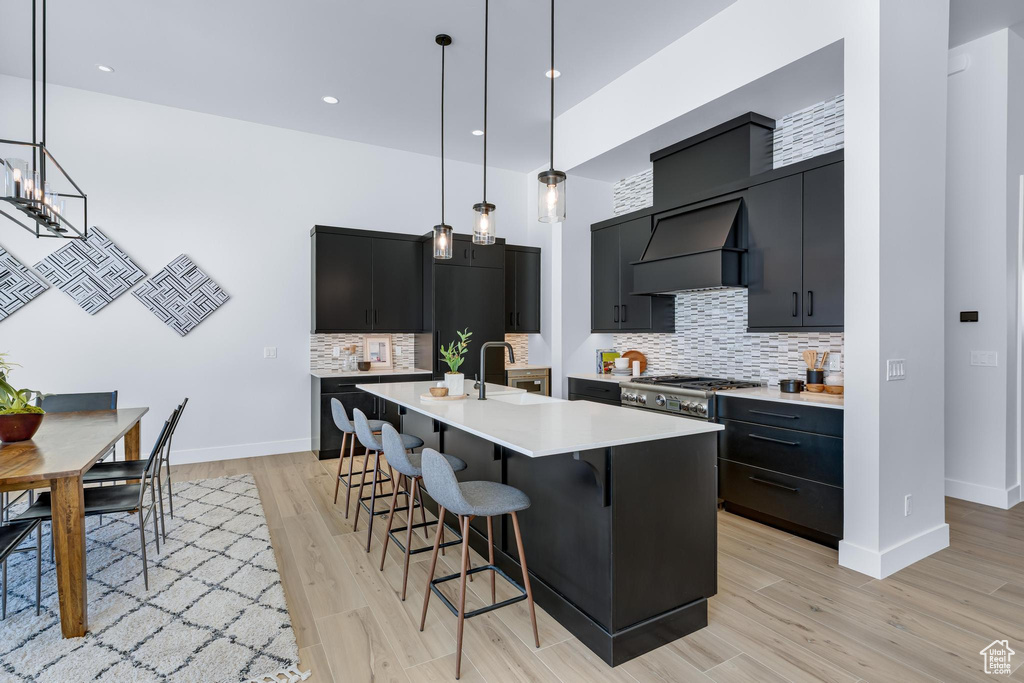 Kitchen featuring pendant lighting, light countertops, an island with sink, and custom exhaust hood