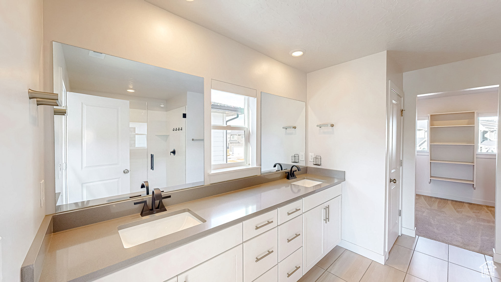 Full bathroom featuring double vanity, a stall shower, a sink, and a walk in closet