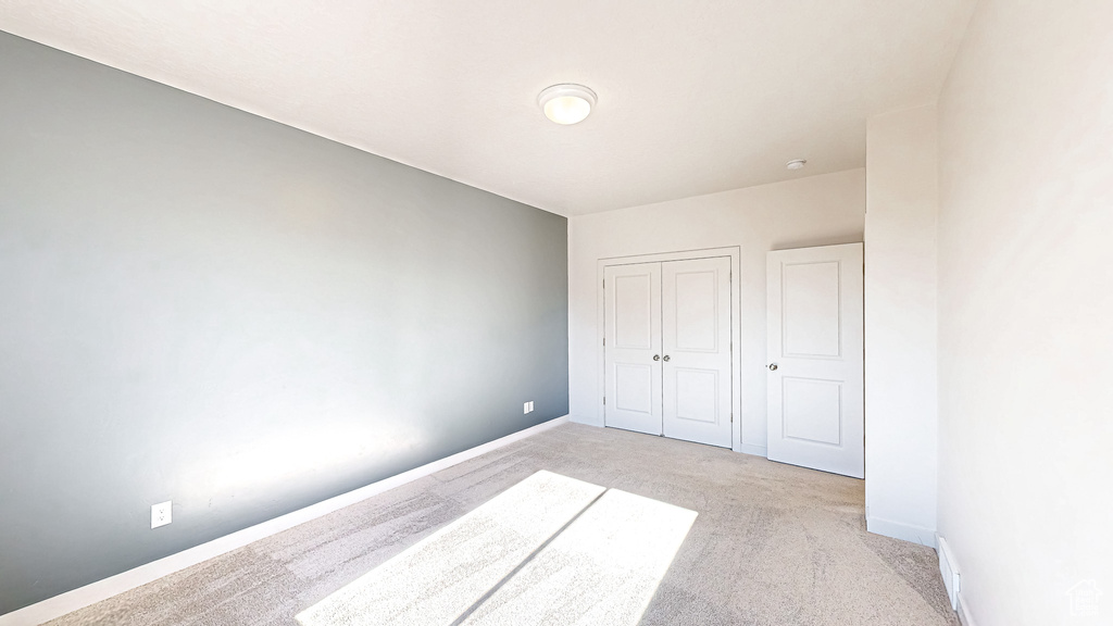 Unfurnished bedroom featuring a closet, light colored carpet, and baseboards