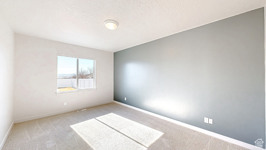 Unfurnished room featuring visible vents, baseboards, a textured ceiling, and light colored carpet