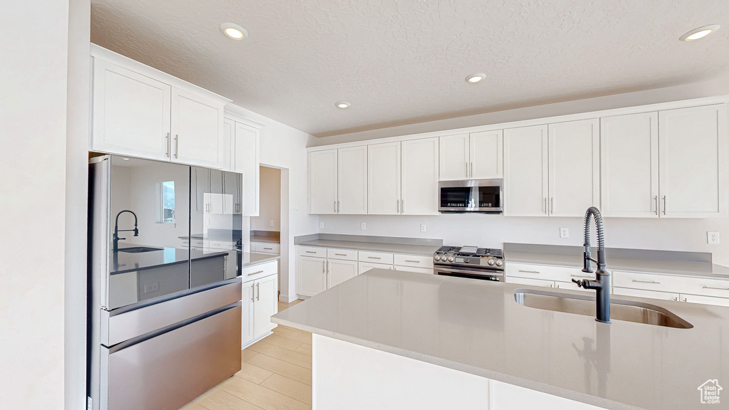 Kitchen featuring stainless steel appliances, light countertops, white cabinets, and a sink