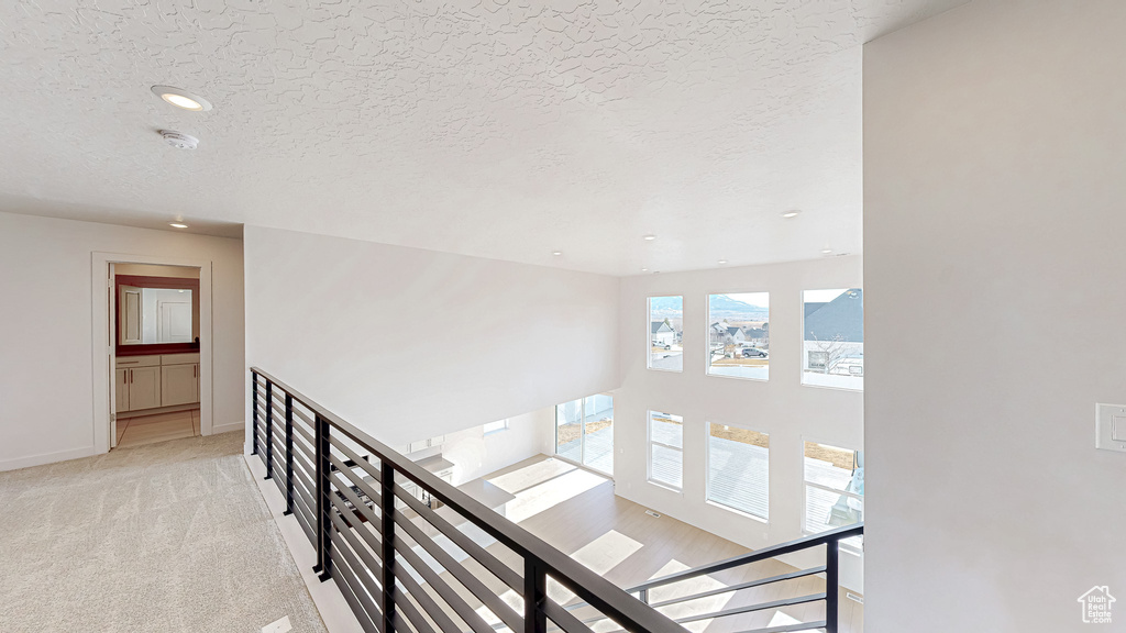 Hall with baseboards, light colored carpet, a textured ceiling, an upstairs landing, and recessed lighting