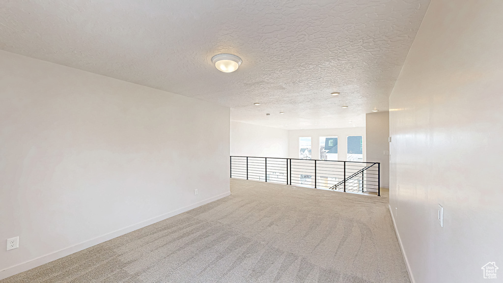 Carpeted empty room with a textured ceiling and baseboards