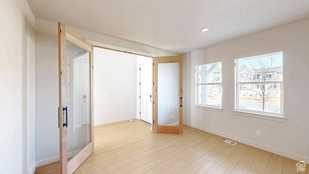 Spare room with light wood finished floors, baseboards, visible vents, and a textured ceiling