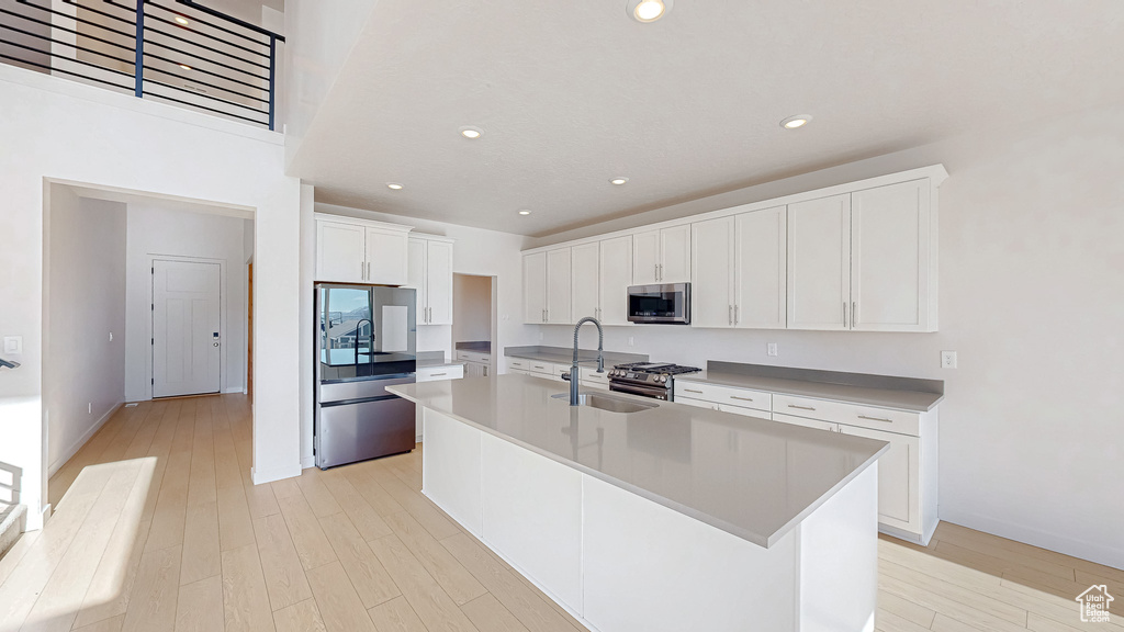 Kitchen featuring white cabinetry, light countertops, appliances with stainless steel finishes, light wood-type flooring, and a center island with sink