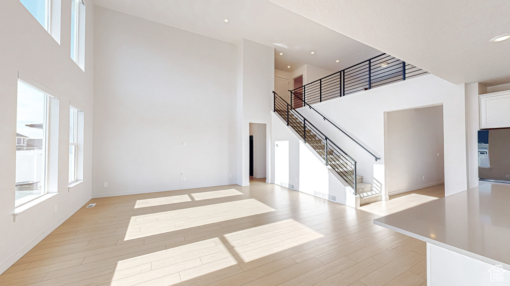 Unfurnished living room featuring light wood-type flooring, stairs, a towering ceiling, and recessed lighting