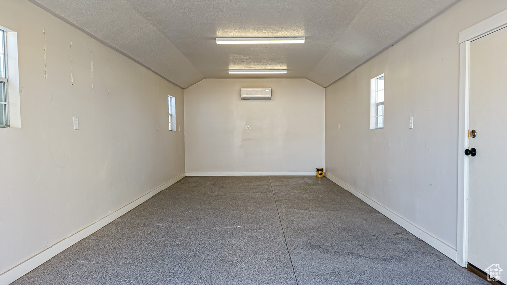 Spare room with baseboards, vaulted ceiling, a textured ceiling, and a wall mounted air conditioner