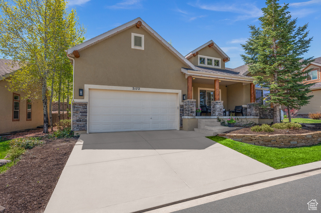View of front of home featuring stone siding, covered porch, driveway, and stucco siding