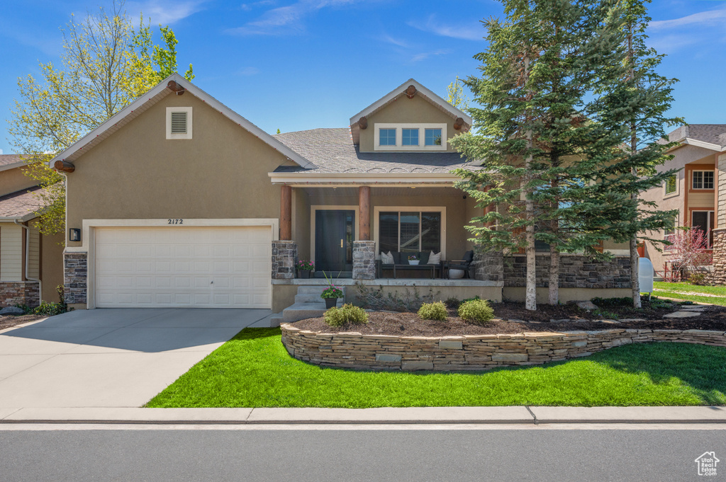 View of front of house with covered porch, stone siding, stucco siding, driveway, and an attached garage