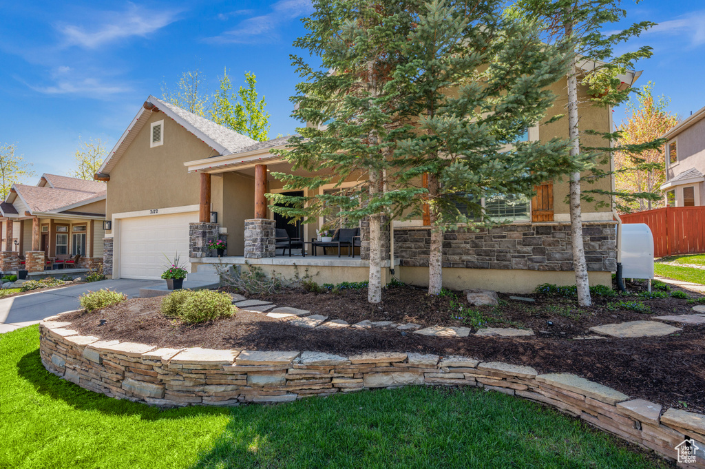 View of front of home with stone siding, stucco siding, a garage, driveway, and fence