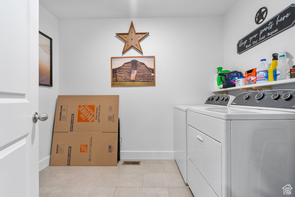 Washroom featuring washing machine and clothes dryer, light tile patterned floors, visible vents, laundry area, and baseboards