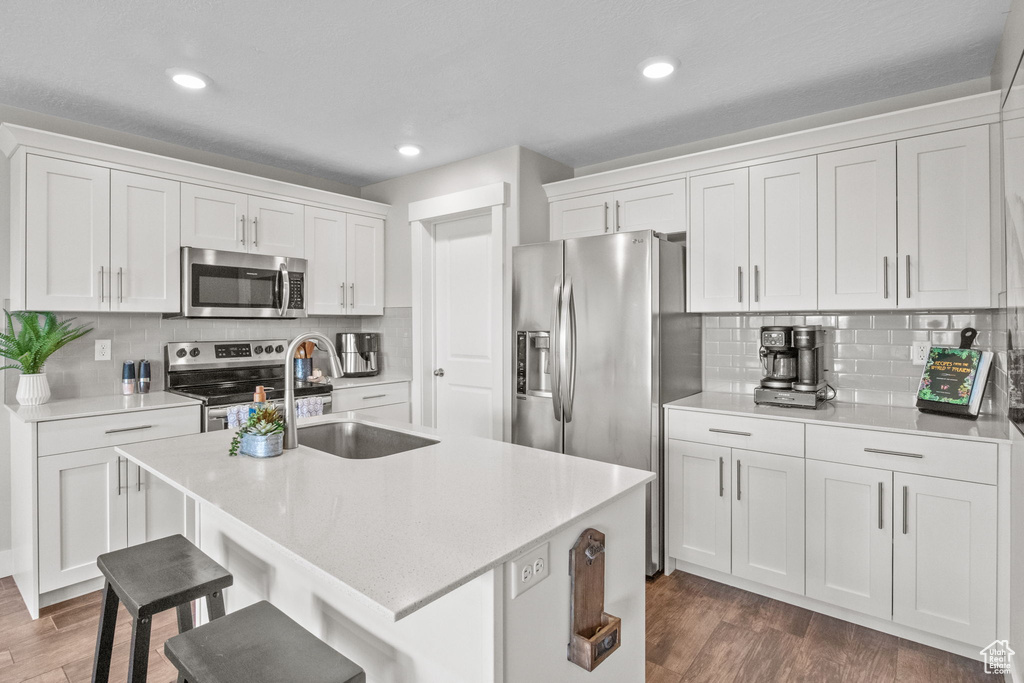 Kitchen with appliances with stainless steel finishes, a sink, white cabinets, light countertops, and recessed lighting