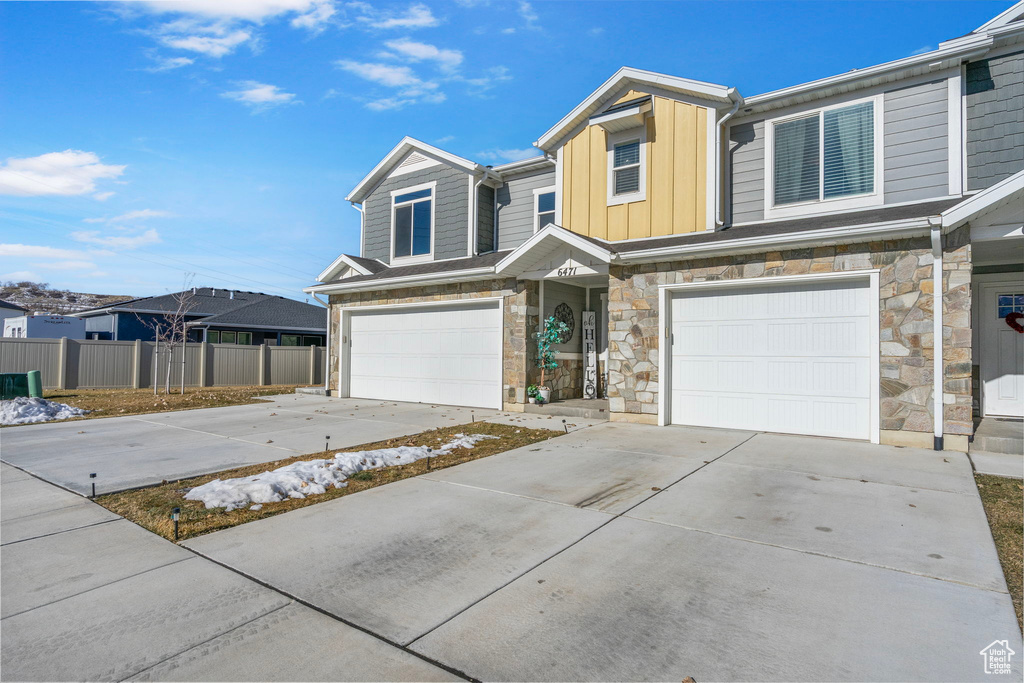 View of property with driveway, board and batten siding, an attached garage, and fence