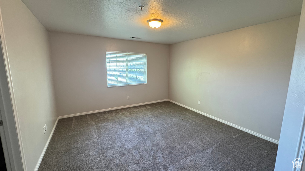 Empty room featuring dark carpet, a textured ceiling, baseboards, and a pendent fire sprinkler
