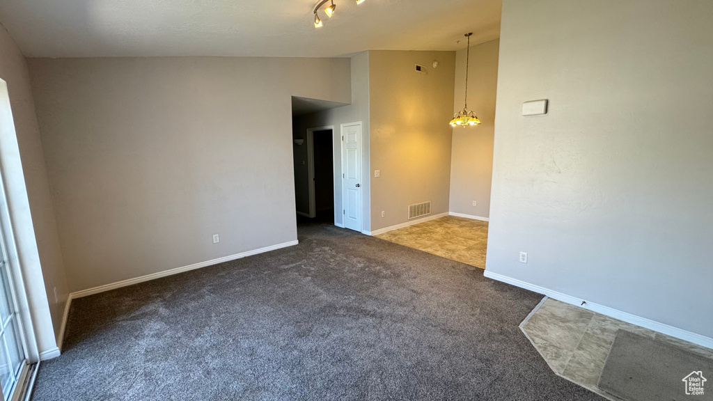 Spare room featuring vaulted ceiling, carpet, baseboards, and a chandelier
