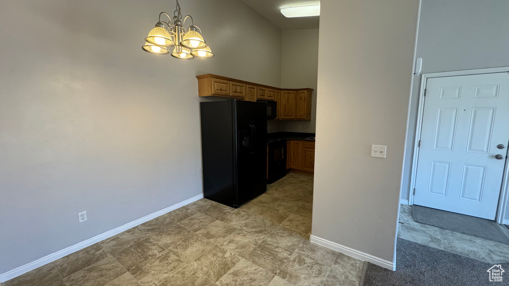 Kitchen with black fridge with ice dispenser, a chandelier, a high ceiling, pendant lighting, and dark countertops