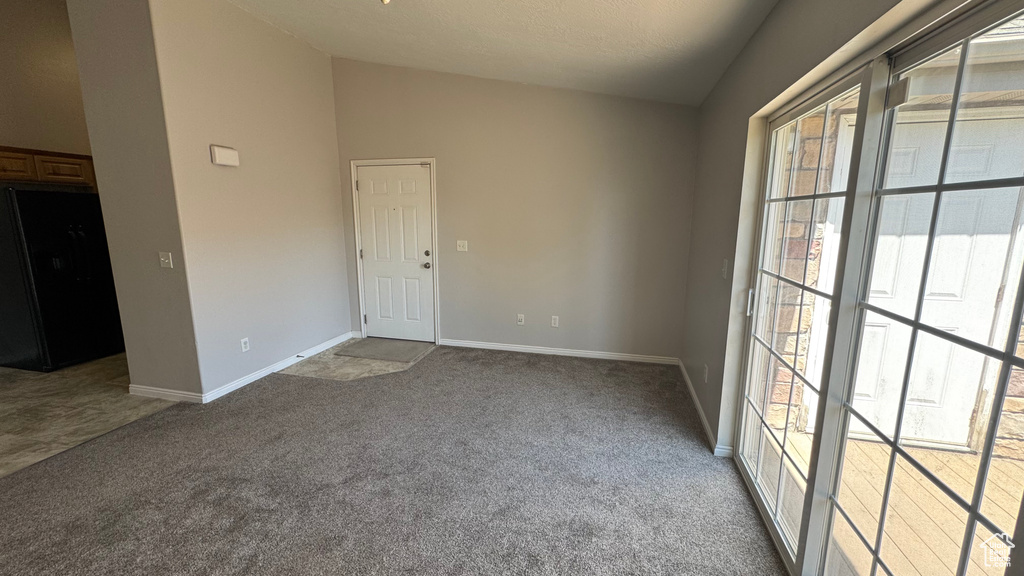 Empty room featuring carpet flooring, healthy amount of natural light, and vaulted ceiling