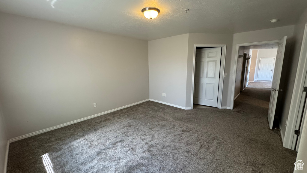 Unfurnished bedroom featuring dark carpet, a textured ceiling, and a closet