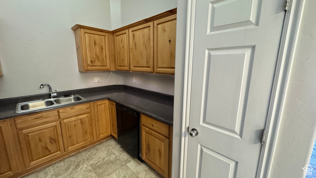 Kitchen featuring black dishwasher, a sink, dark countertops, and brown cabinets