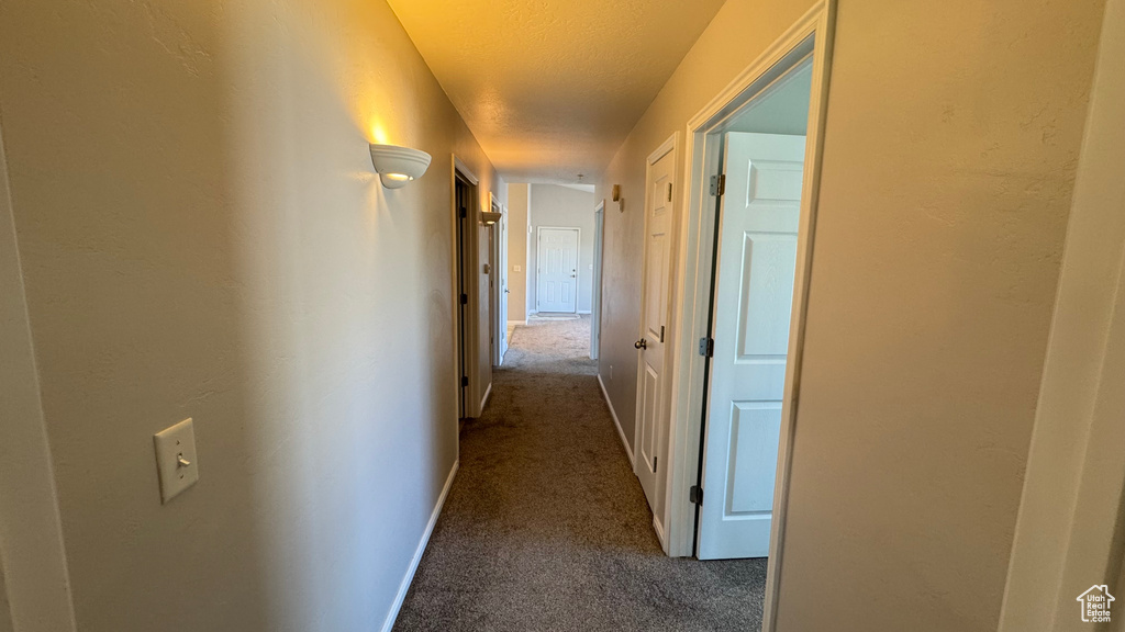 Hallway featuring dark colored carpet, baseboards, and a textured ceiling