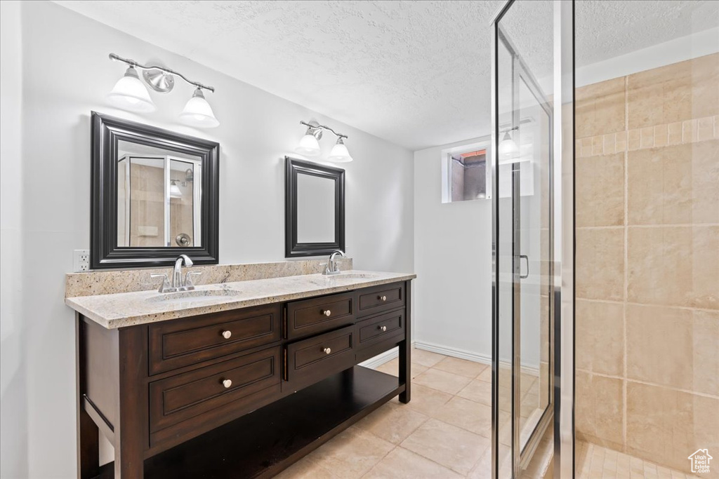 Full bath with a textured ceiling, double vanity, a stall shower, and a sink
