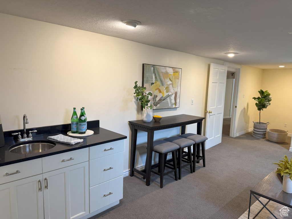 Kitchen with a sink, dark countertops, dark carpet, white cabinets, and baseboards
