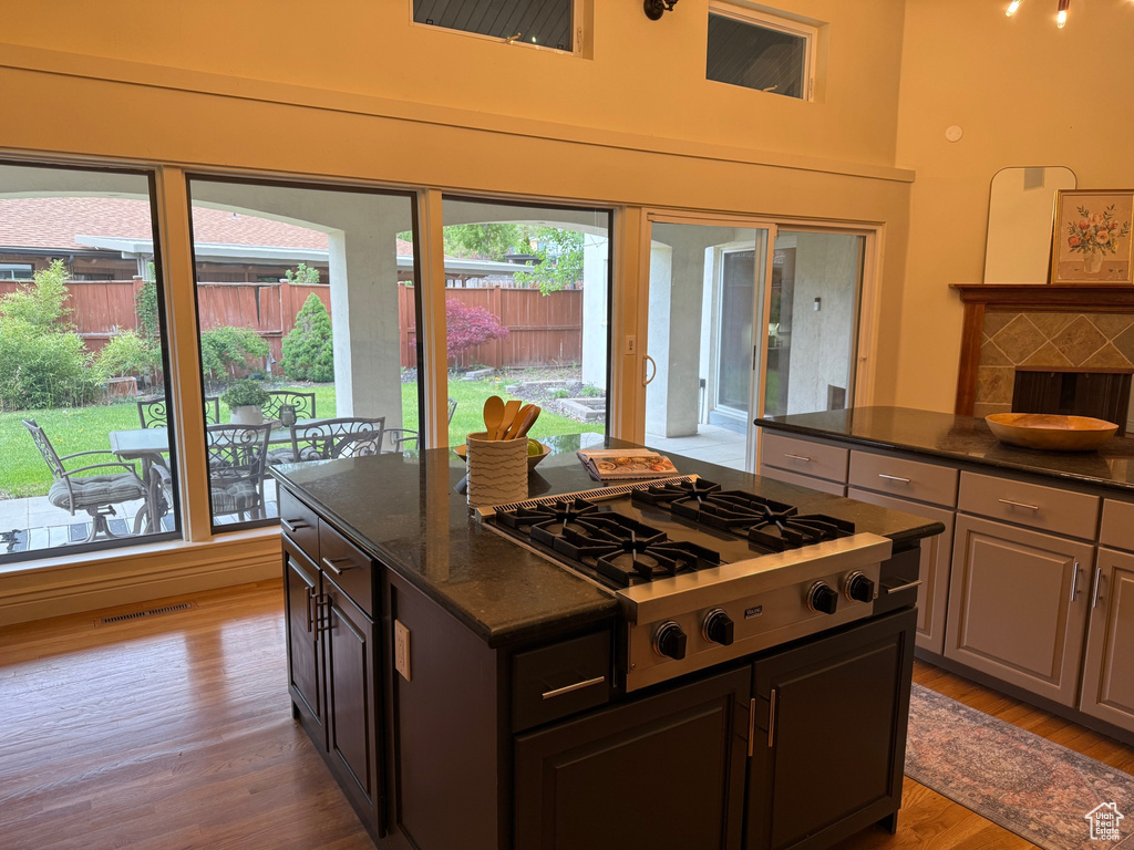 Kitchen with stainless steel gas cooktop, wood finished floors, a center island, dark stone countertops, and a towering ceiling