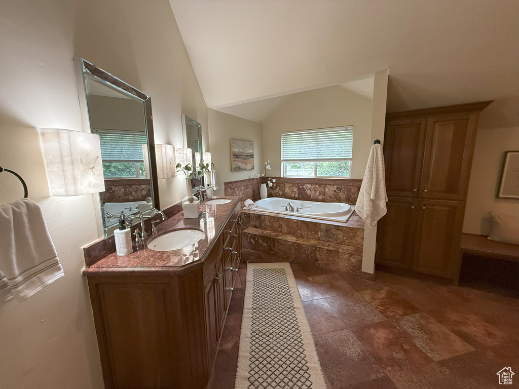 Bathroom featuring a bath, double vanity, a sink, and vaulted ceiling