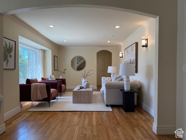 Living area featuring crown molding, arched walkways, baseboards, and wood finished floors