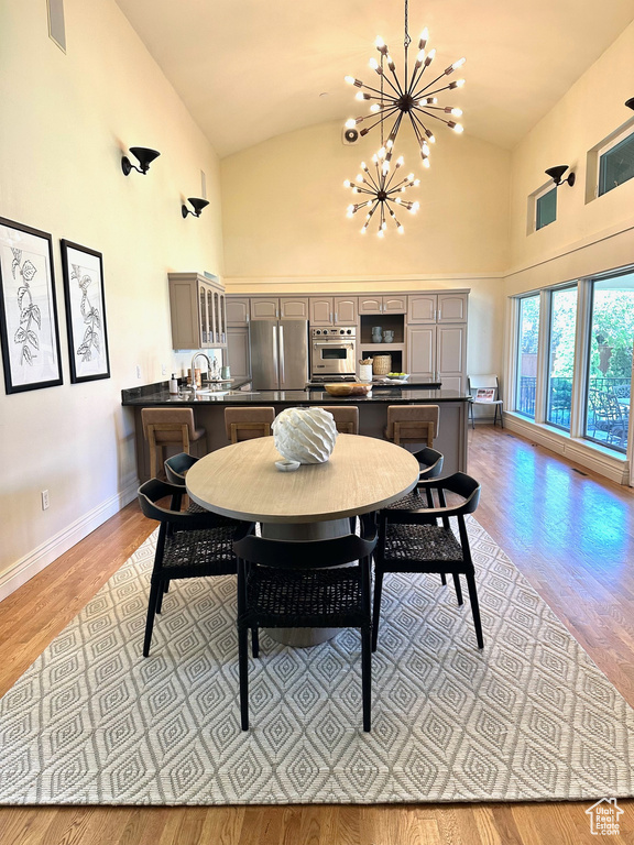 Dining room with visible vents, high vaulted ceiling, baseboards, light wood finished floors, and an inviting chandelier