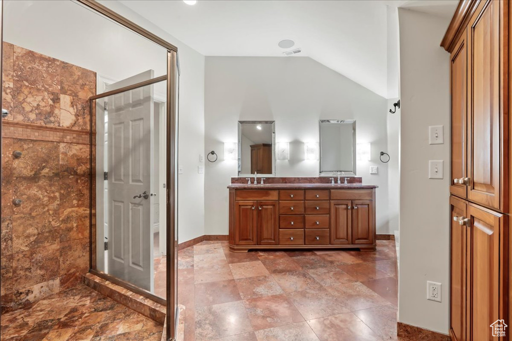 Bathroom featuring double vanity, a shower stall, baseboards, and vaulted ceiling