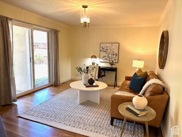 Living room featuring baseboards, a chandelier, ornamental molding, and wood finished floors