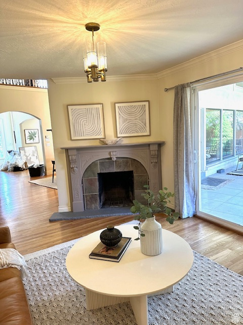 Living room with a chandelier, ornamental molding, wood finished floors, and a fireplace