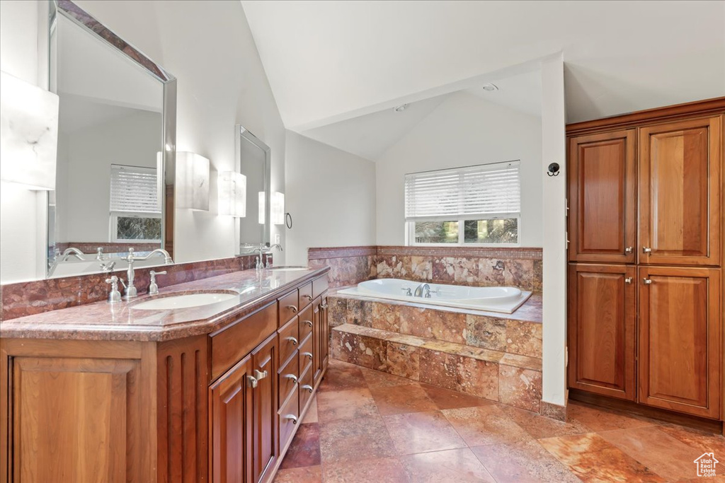 Bathroom with lofted ceiling, double vanity, a sink, and a bath