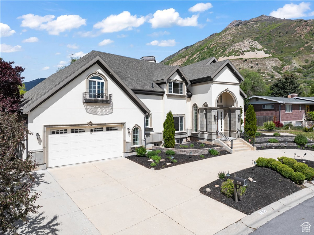 French country home with roof with shingles, a garage, a mountain view, concrete driveway, and stucco siding