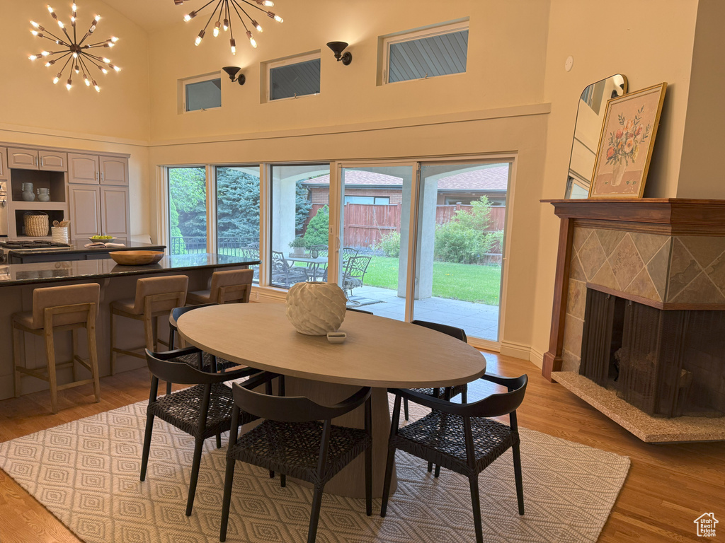 Dining room with a tile fireplace, light wood-style floors, a chandelier, and high vaulted ceiling