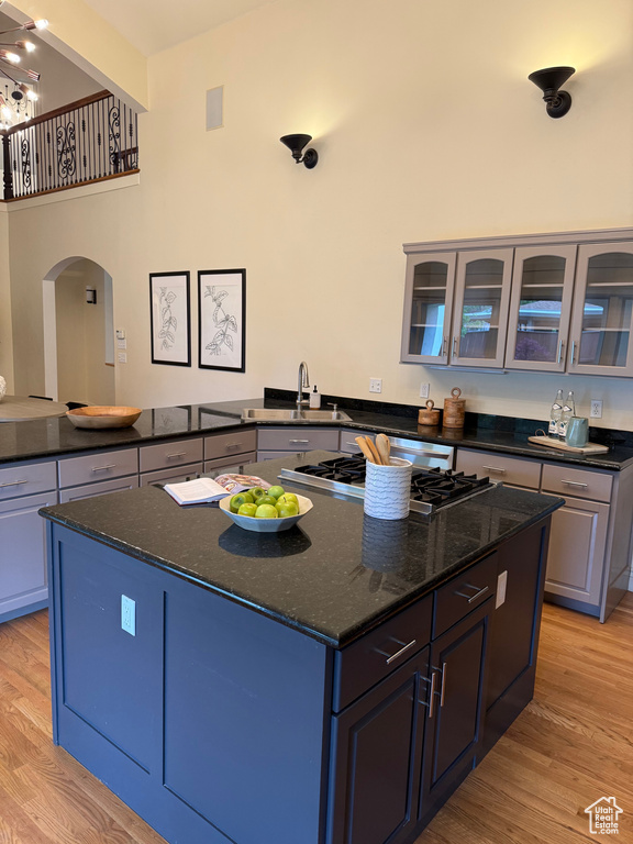Kitchen with stainless steel gas stovetop, light wood-type flooring, arched walkways, a center island, and glass insert cabinets