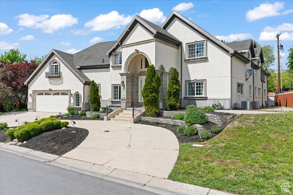 View of front of house featuring central AC, a front lawn, a garage, stucco siding, and curved driveway