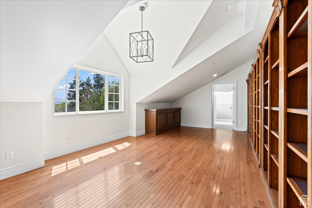 Additional living space featuring a chandelier, lofted ceiling, light wood-style flooring, and baseboards