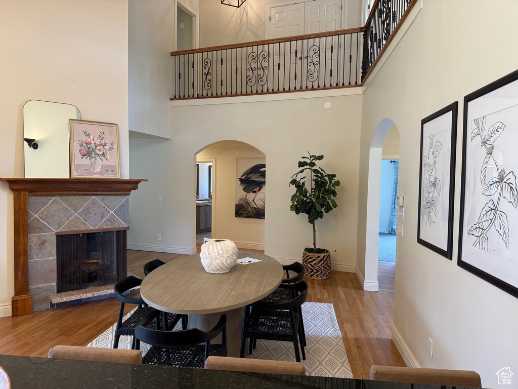 Dining room with arched walkways, a towering ceiling, wood finished floors, a fireplace, and baseboards