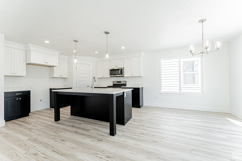 Kitchen featuring appliances with stainless steel finishes, a chandelier, white cabinetry, baseboards, and light wood-style floors