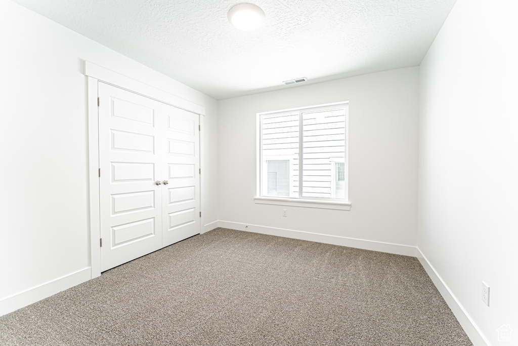 Unfurnished bedroom featuring carpet floors, a textured ceiling, baseboards, and a closet