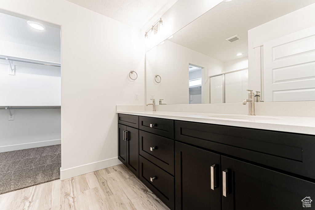 Full bath with double vanity, a shower stall, a walk in closet, baseboards, and wood finished floors