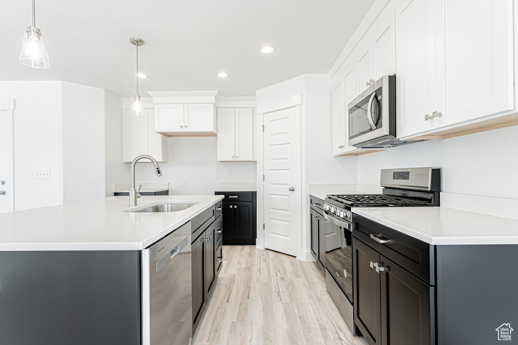 Kitchen with appliances with stainless steel finishes, a sink, light wood-style floors, recessed lighting, and white cabinets